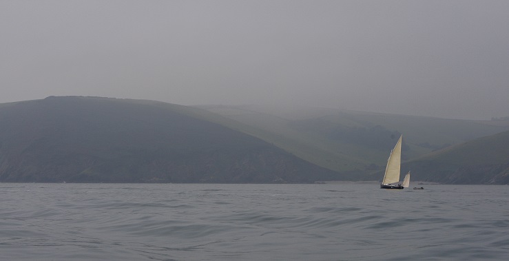 A small boat is sailing along a foggy stretch of water.