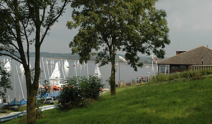 a beautiful exterior of a sailing club next to a lake and some trees
