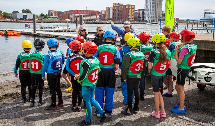 wide shot a large group of pre-teens listing to an instructor next to a lake