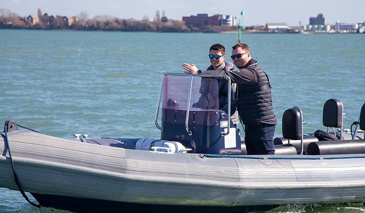 wide shot of two people standing in a motorboat on the water, they are both smiling