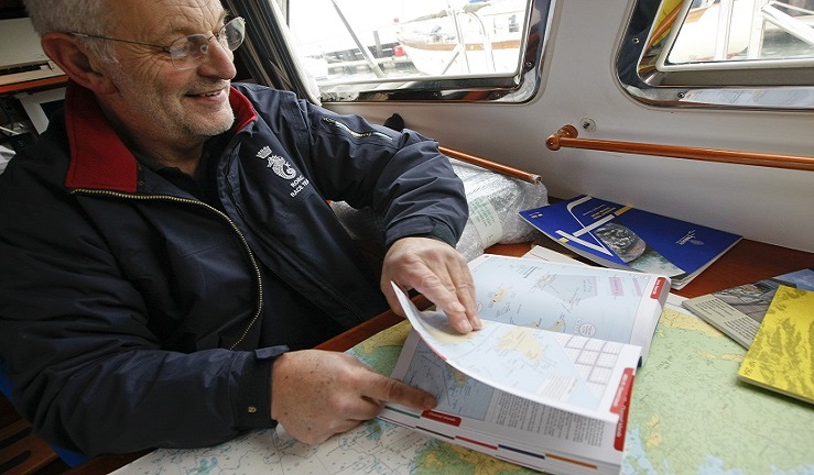 A man is looking at charts and a book below deck