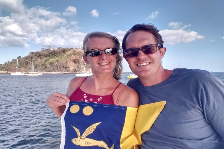 A woman and a man are proudly holding a flag depicting the logo of the Ocean Cruising Club