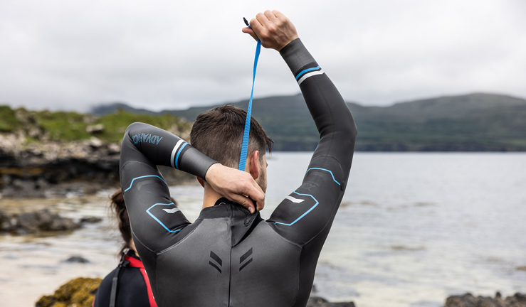 RYA member offers Cotswold. Back of mans head and shoulders, he is reaching over his head to zip up wetsuit. 