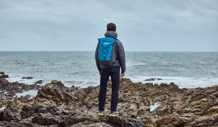 RYA member offers Gill. Man stood on rocks looking out at sea. He is wearing a Gill rucksack.