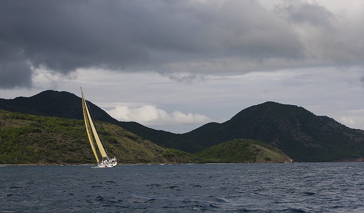 A yacht is sailing under a stormy sky with green mountains in the background