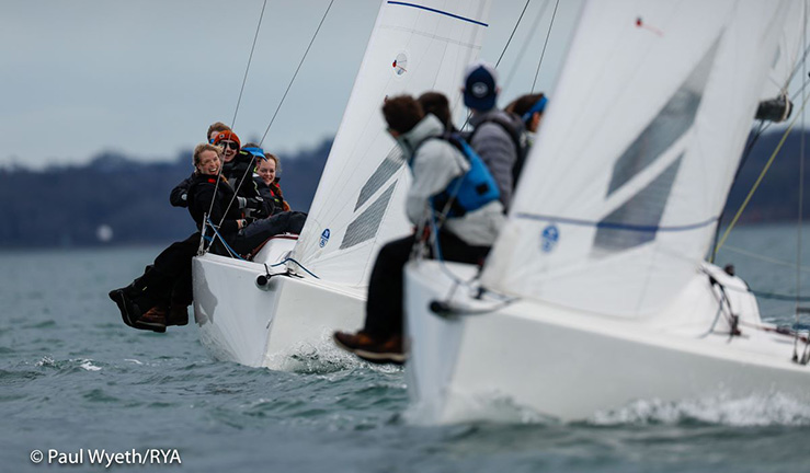 Two J70 keelboats being sailed up wind with crew from the British Keelboat Academy who are smiling at each other and for the camera.