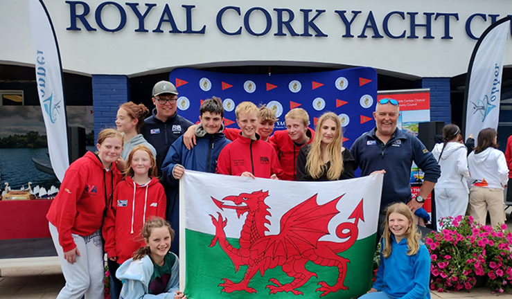 Group Topper sailors with their coaches and the Welsh flag having a team photo in front of Royal Cork YC at the Topper Worlds 2023.