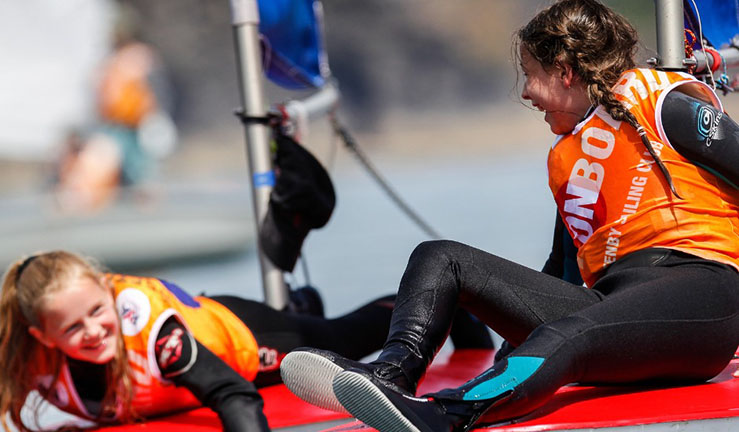 Two girls wearing orange OnBoard bibs having fun on Topper dinghies on a sunny day. 