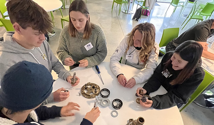 Five young sailors problem-solving at a table with winch components in Harken hardware workshop at North Sails during British Keelboat Academy selection weekend.