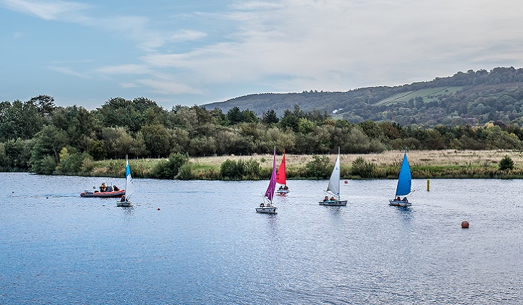 Five dinghies and a safety boat are sailing across a lake