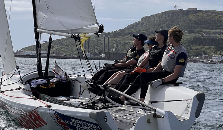 Skipper Ben Tylecote and his team from Rutland SC sailing an Elliott 6m with Portland in the background at the RYA Harken Youth Match Racing Championship 2023