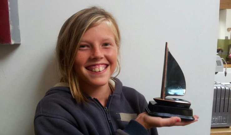 Young Meg smiling and holding a dinghy-shaped trophy