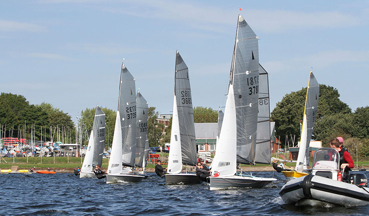 Fleet of Merlin Rockets racing at Bartley SC with clubhouse in background.