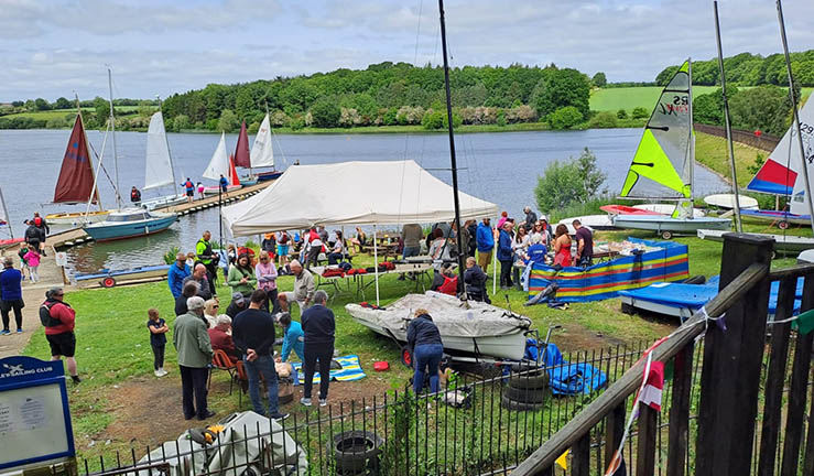 View over Cransley SC lake with lots of dinghies and people visiting for the club's Discover Sailing open day.