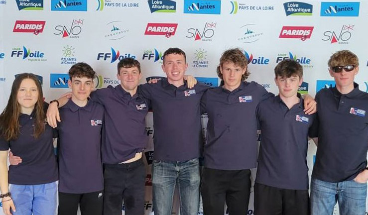GBR teams on shore with 7 sailors in front of logo background at Eurosaf Youth Match Racing European Championship in Nantes, France, 2023