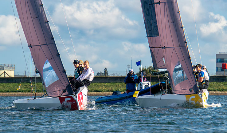 Two teams racing RS21s upwind with an umpire RIB and committee boat in the background on a sunny day at the RYA National Match Racing Grand Finals 2023.