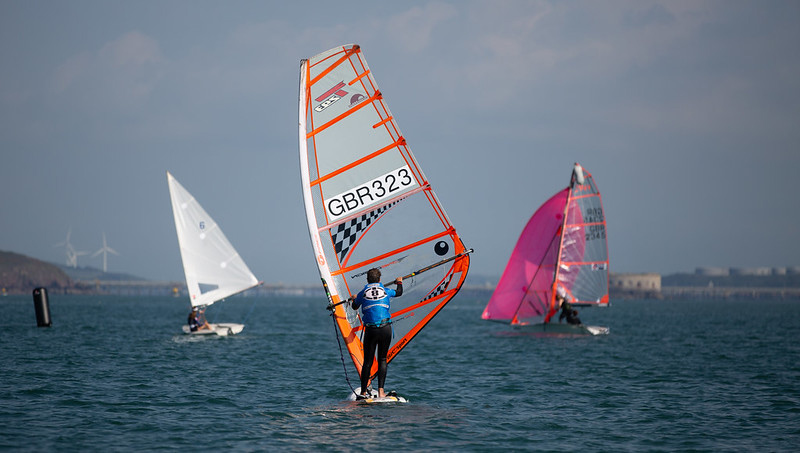 A windsurfer and two dinghies on the water in the sunshine.