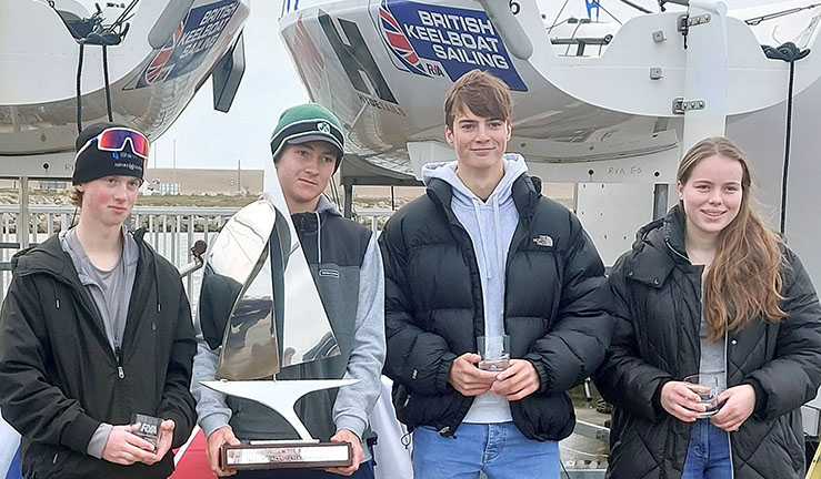 Winning team of four - 3 boys and a girl - on shore at WPNSA with large shiny boat shaped trophy after winning RYA Schools Match Racing Championship 2023