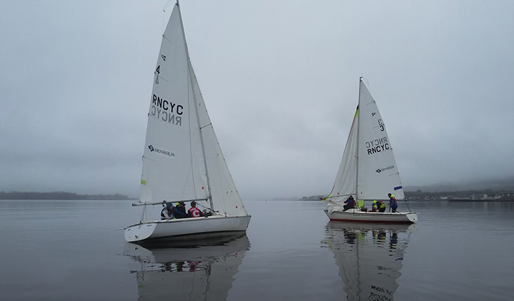 Two Sonar keelboats racing in very light wind and mist on a grey day with reflection of each boat and its sails on the water - atmospheric picture at Royal Northern & Clyde YC for the 2023 Ceilidh Cup match racing event.