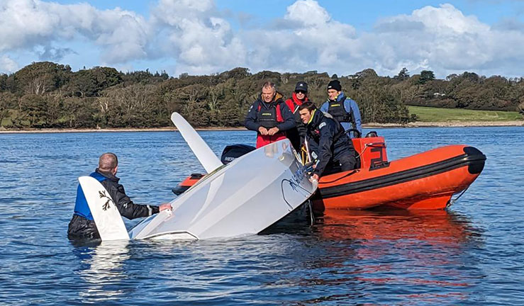 Four people on an orange RIB lifting an inverted dinghy onto the side with someone in the water, in a safety boat skills session at The Big Weekend for clubs, training centres and instructors at Plas Menai.