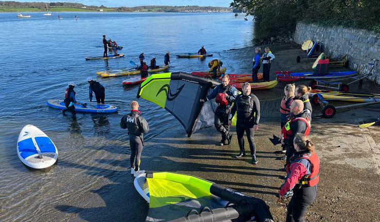 Lots of people on shore and just launching onto the water in the sunshine at Plas Menai for a winging and SUPing session as part of The Big Weekend for clubs, training centres and instructors.