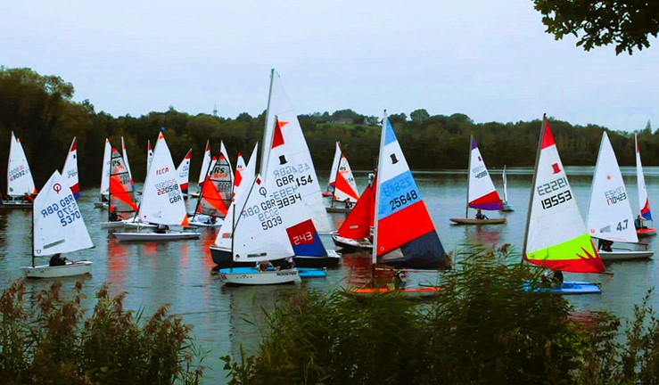 A lake full of colourful youth and junior sailing dinghies racing on a grey day in light winds at Ripon Sailing Club for the North East & Yorkshire Youth Traveller Series 2023.