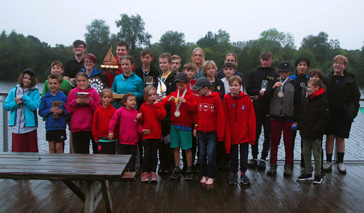 A group of 20+ young sailors with medals and trophies outside on a grey day for a prizegiving photo at Ripon Sailing Club the end of the North East & Yorkshire Youth Traveller Series.