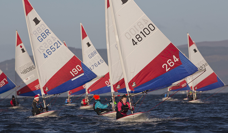 A fleet of Topper dinghies racing with low sunlight and a few Santa hats. 