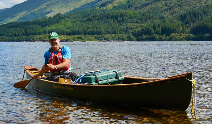 Adventurer and guiding expert Myles Farnbank on the water paddling a canoe with mountains in the background.