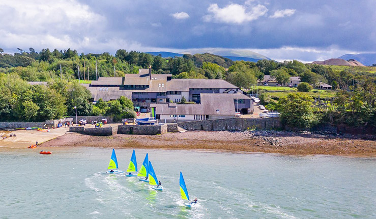 Drone view over Plas Menai National Outdoor Centre for Wales with five dinghies sailing in the foreground.