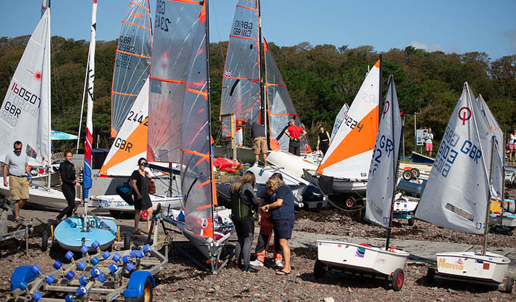 Variety of youth and junior boats with sails up on shore on a sunny day at Dale waiting to launch for the RYA Cymru Wales OnBoard Festival. 