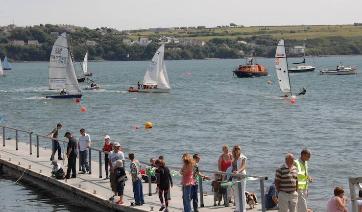 Lots of boats and people on a pontoon enjoying a sunny day on the water.