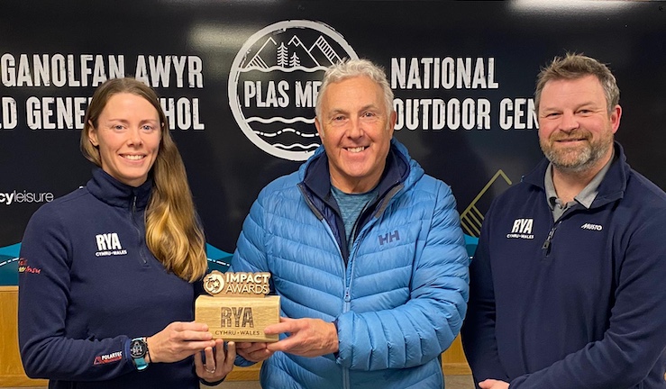 RYA Cymru Wales Performance Manager Sarah McGovern (left) presents an Impact Award to Jamie Johnson (centre) who is flanked by CEO James Stuart (right) with Plas Menai branded wall as a backdrop.