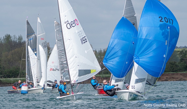 Around six dinghies racing at Notts County SC at the start of the season with the two boats at the front flying blue spinnakers.