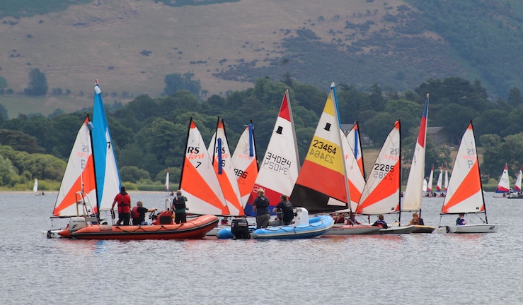 Group of a dozen or so junior dinghies with colourful sails gathered around two RIBs with hillside in the background at a previous BYS North Regional Junior Championships.