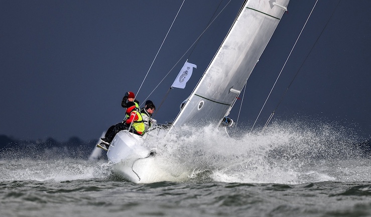 Sun Fast 30 One Design in action offshore with the RORC Griffin Project, sailing upwind towards the camera with white water splashing from the bow and a near black sky behind.