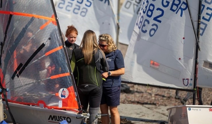CW Chair Sian Reynolds chatting to a couple of sailors on the shore next to a rigged 29er and Optimist dinghies.