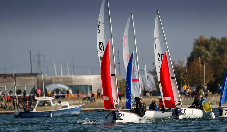 Firefly dinghies coming off the startline with red and blue jibs on a sunny day at a team racing event hosted by Oxford Sailing Club.