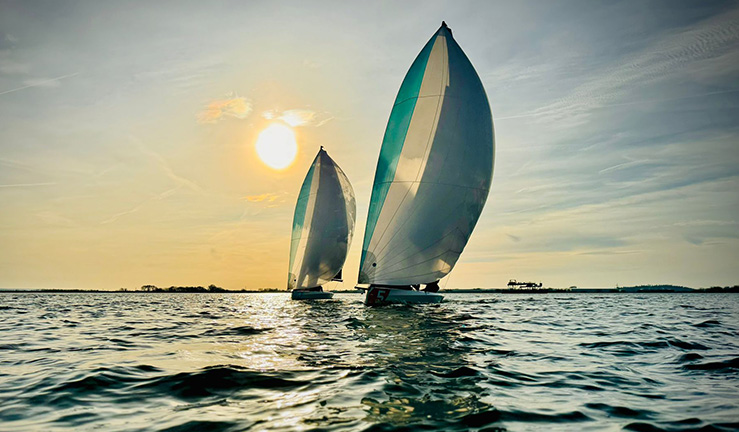 Two keelboats flying spinnakers with low winter sun casting a glow over the sails and water at Queen Mary Sailing Club.