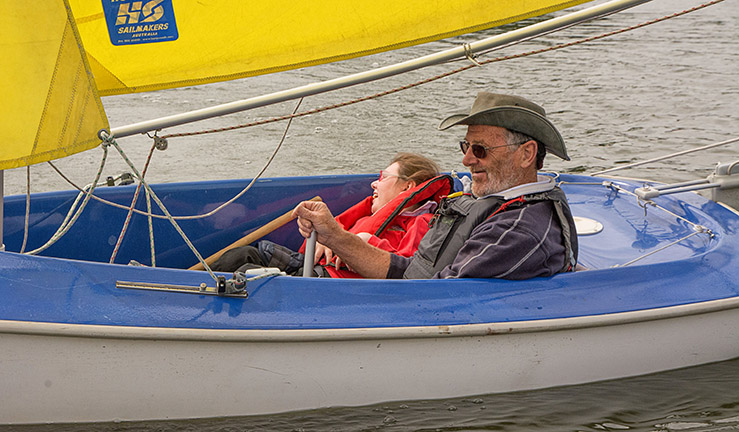 Sailor and crew in a blue Sailability access boat with yellow sails on the water at Gresford SC.
