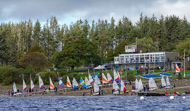 View of Derwent Reservoir Sailing Club from the water with lots of dinghies on the shore about to launch for the Regional Junior Championships in 2019.