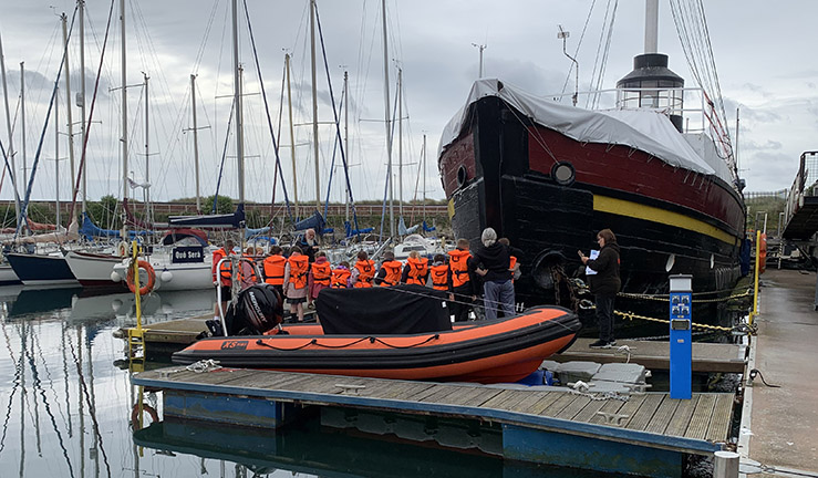 Group of school children wearing orange lifejackets learning about HY Tyne Lightship in the dock. 