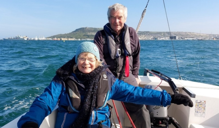 An older female and older male sailing a Hawk on the open sea, smiling at the camera