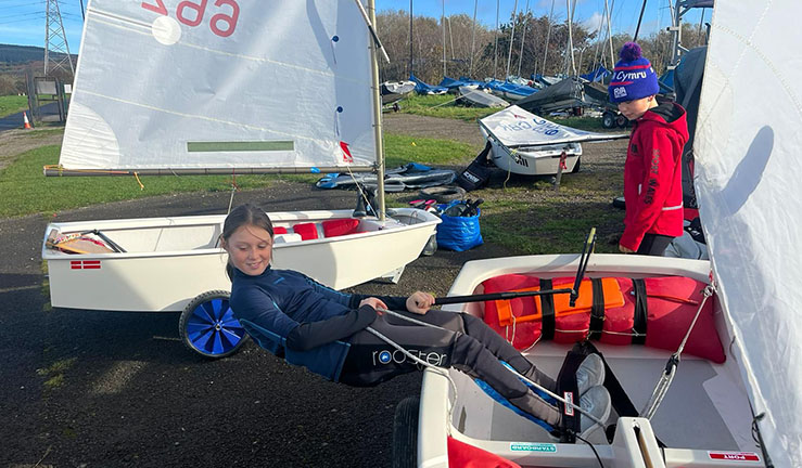 An Optimist sailor practising hiking in a boat on shore as part of Welsh squad winter training.