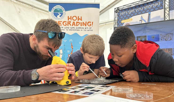 Two school children are looking at petri dishes with an adult