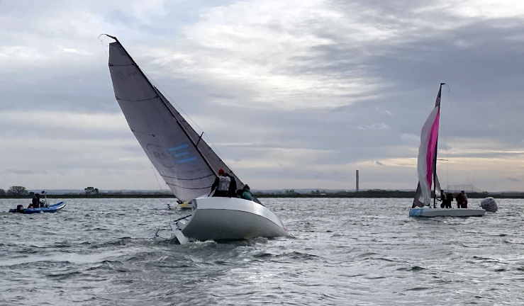 RS21 keelboat heeled well over and heading upwind with another RS21 and a race officials RIB in the background on a grey day during match racing at Queen Mary SC for Qualifier 1 of the RYA 2024 series.