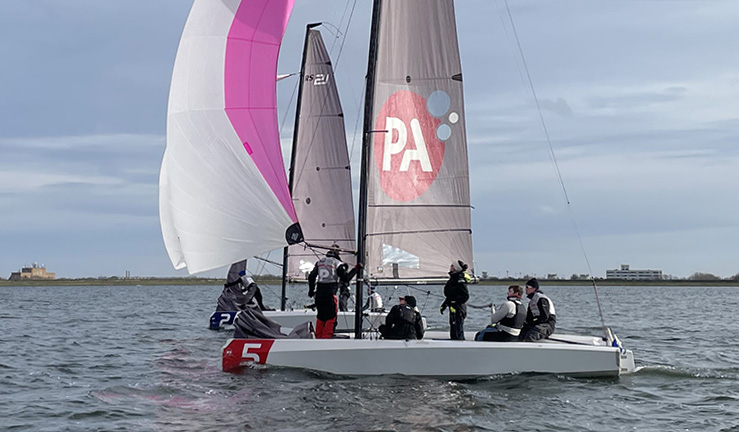 Side view of two RS21s neck and neck match racing downwind with pink and white spinakers flying.
