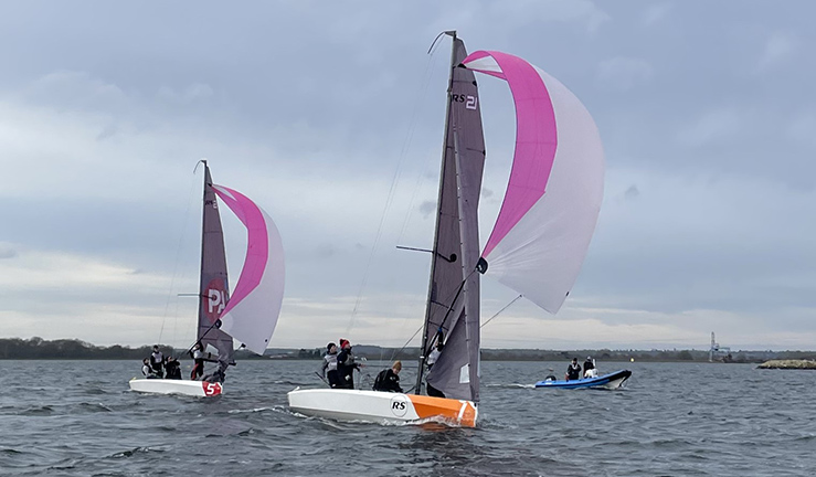Two teams match racing aboard RS21s with pink and white spinnakers flying on a grey day at Queen Mary SC.