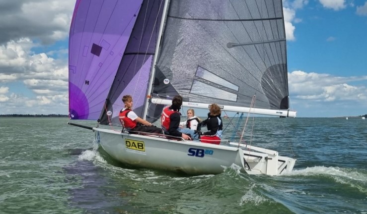 Young sailors from the team 'Teen Spirit' sailing an SB20 downwind with a purple spinnaker flying on a sunny day with blue skies during Qualifier 4 of the British Keelboat League on the Blackwater Estuary.