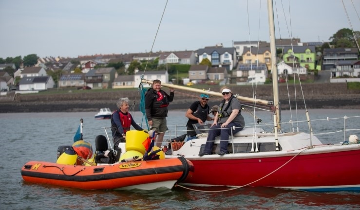 A red and white yacht with three people aboard and an orange RIB alongside with flags and buoys for Neyland YC regatta and Dragon Series.